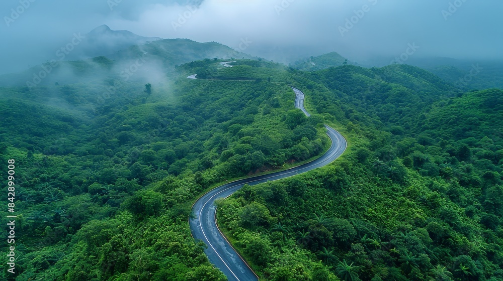 Fototapeta premium Aerial view of a curvy mountain road surrounded by dense fog and vibrant green forest Perfect for illustrating travel and nature themes