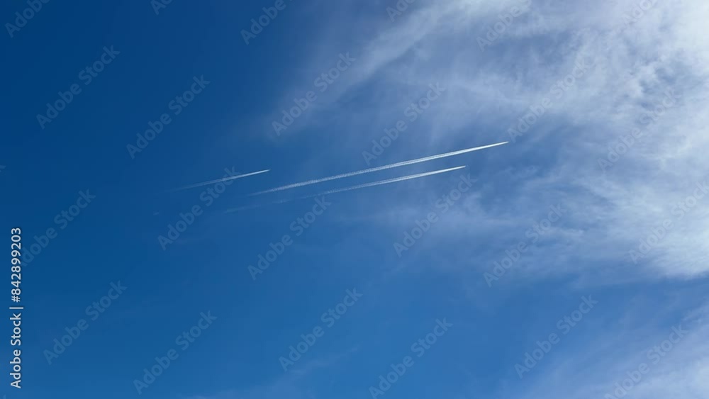 Three distant jet planes fly high, leaving white trace of contrail against the background of a blue sky with clouds, at a sunny day Three distant jet planes fly high, leaving white trace of contrail against the background of a blue sky with clouds, at a sunny day