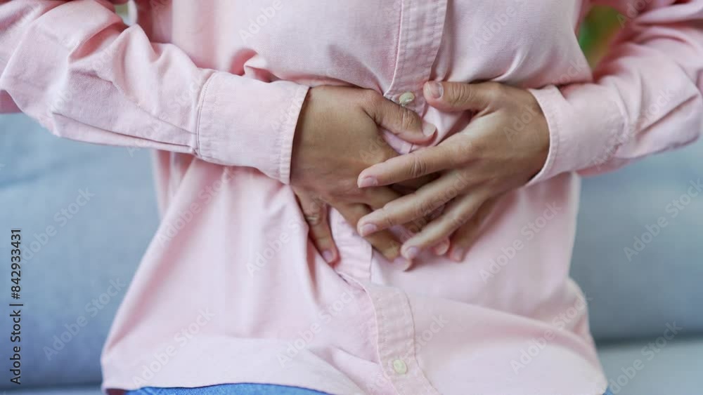 Close up. Female hands massaging the stomach. Young black woman suffering from abdominal pain while sitting on sofa in living room at home. She has poisoning, constipation, spasms or menstruation Close up. Female hands massaging the stomach. Young black woman suffering from abdominal pain while sitting on sofa in living room at home. She has poisoning, constipation, spasms or menstruation