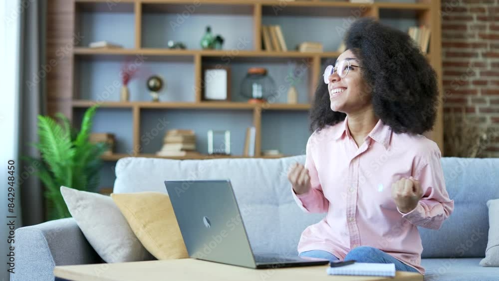Shocked happy young african american female reading great news on laptop sitting on sofa at home office. Excited black woman freelancer celebrating success, satisfied with positive message on computer