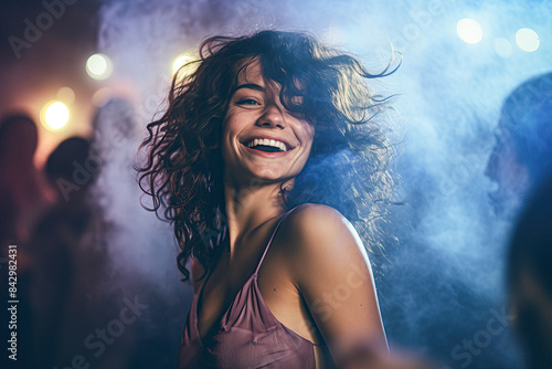 A woman with curly hair is smiling and dancing in a club © Kowit