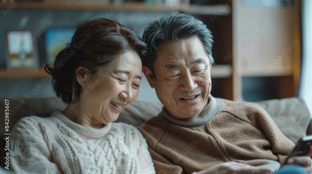 Senior japanese couple sitting on a couch , relaxed , and spending time together ,looking at a cell phone Senior japanese couple sitting on a couch , relaxed , and spending time together ,looking at a cell phone