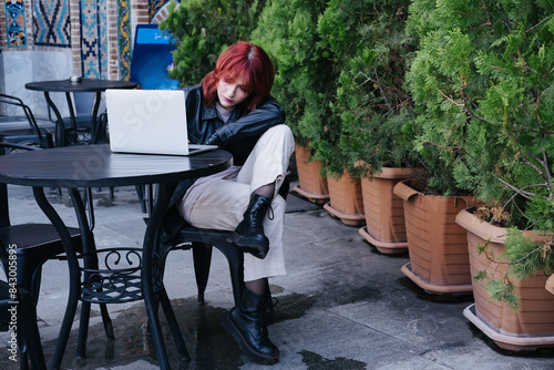 Young woman model mix race with red hair sitting in cafe outdoor with laptop