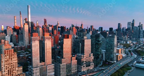 Blue skies with slightly seen clouds above the downtown of New York, the USA. Distancing from the city buildings reflecting pink light.
