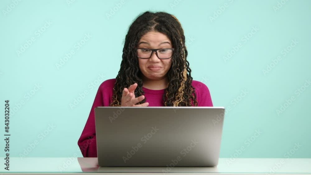 A cheerful woman with glasses and curly hair is working on her laptop in a welllit room, displaying different expressions. She seems content and engaged, creating a positive work environment A cheerful woman with glasses and curly hair is working on her laptop in a welllit room, displaying different expressions. She seems content and engaged, creating a positive work environment