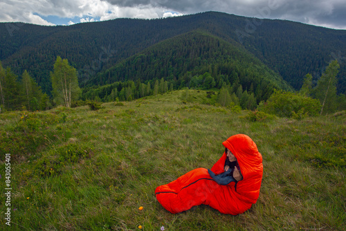 Woman tourist in orange sleeping bag  on green grass in Carpathian mountains photo