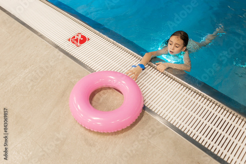 Closeup portrait of little swimmer girl take a rest after swimming in the swimming pool. Little girl is afraid of drowning in the water. Copy space. Children's safety concept near the pool water