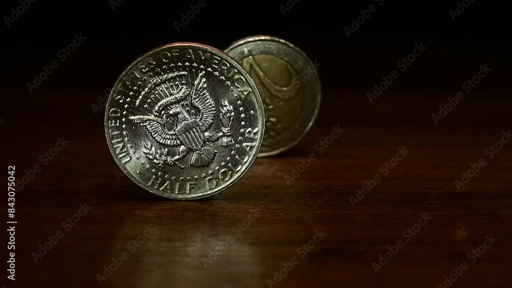 a half US dollar, 50 cent coin rolls across the table and overtakes a two euro coin a half US dollar, 50 cent coin rolls across the table and overtakes a two euro coin