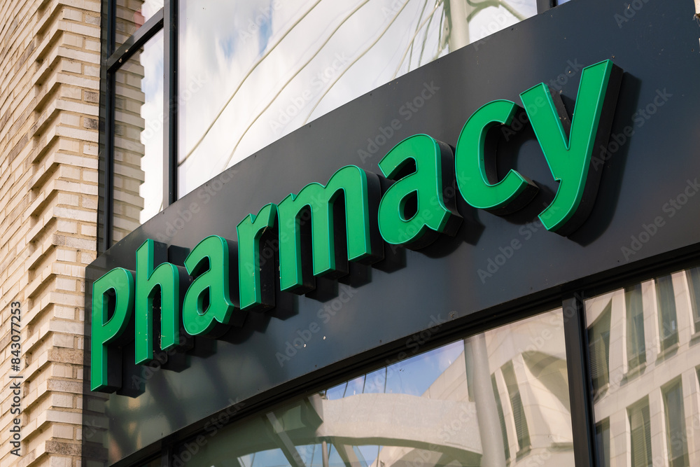 Obraz premium Pharmacy logo sign on a building facade. Drugstore advertisement in big green colored letters. Retailer for pharmaceuticals and medicine in a European city.
