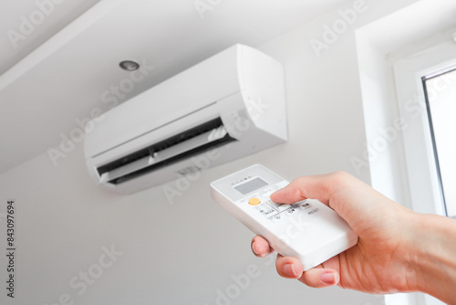 Air conditioner temperature adjustment with remote controller in room at home. Hand holding remote controller of air conditioner inside the white room and set at cool temperature