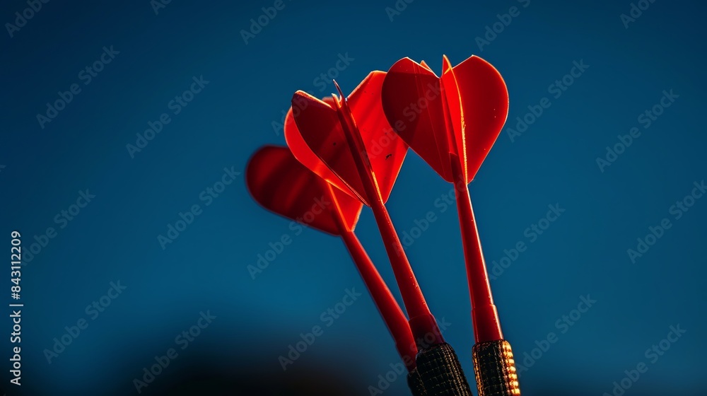 A close-up photograph captures red dart arrows hitting the center of the target against a dark blue sky background. This imagery symbolizes the success and achievement of business targets A close-up photograph captures red dart arrows hitting the center of the target against a dark blue sky background. This imagery symbolizes the success and achievement of business targets