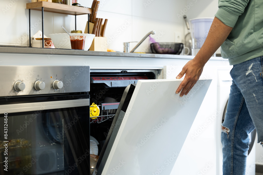 young man putting a dishwasher in his house after a meal. Closing the dishwasher door to turn it on. Man doing housework.