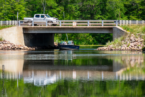 A fishing boat passes under a bridge while a truck crosses the bridge from above. photo