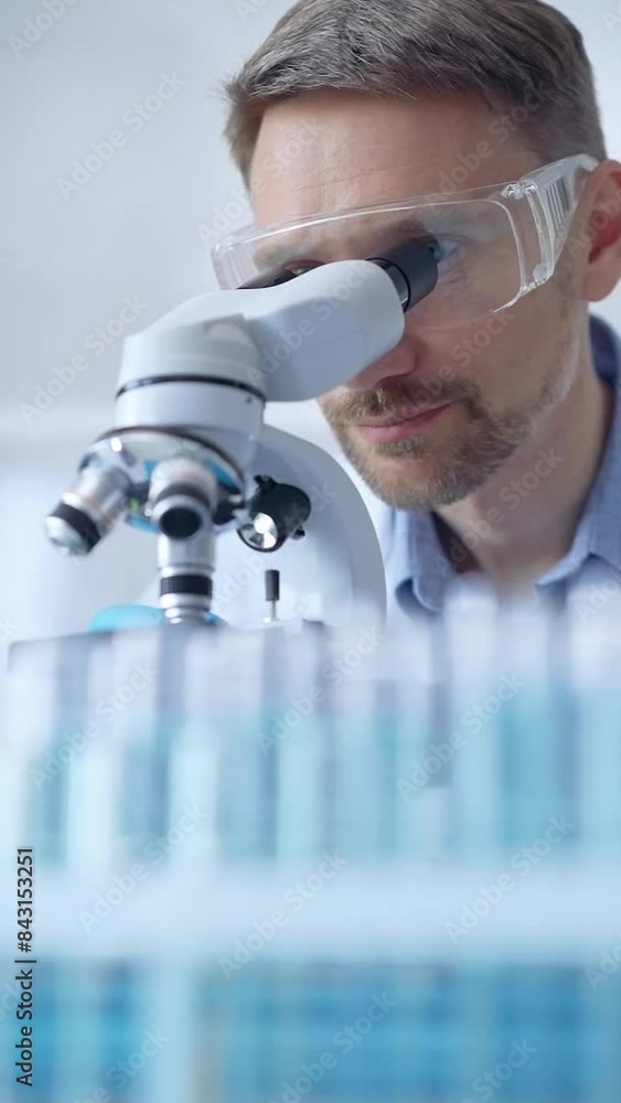 Man scientist with protective glasses and gloves is using microscope in laboratory, vertical portrait of researcher. Microbiology science concept Man scientist with protective glasses and gloves is using microscope in laboratory, vertical portrait of researcher. Microbiology science concept