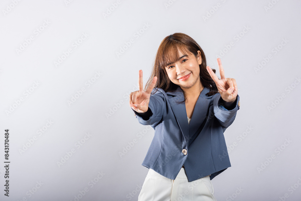 An Asian woman expresses her optimism and peace by forming victory and peace signs near her eye. This studio shot on a white background radiates positivity and success. An Asian woman expresses her optimism and peace by forming victory and peace signs near her eye. This studio shot on a white background radiates positivity and success.