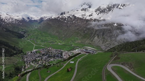 The alpine village of Andermatt surrounded by green meadows, and snowy peaks in the background, Canton of Uri, Switzerland, Europe