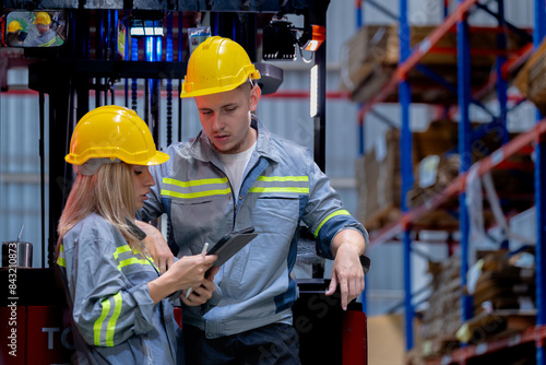 Two male and female factory checkers are discussing work on a warehouse truck. While working in a warehouse for industrial products