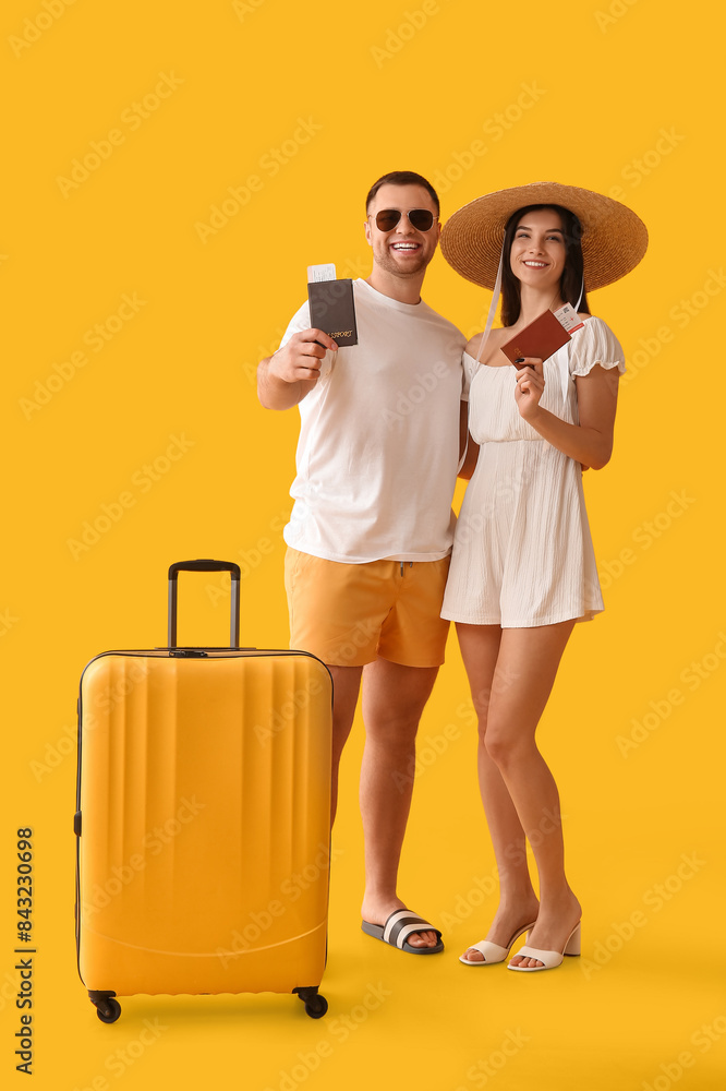 Beautiful young happy couple of tourists with suitcase, passports and tickets on yellow background Beautiful young happy couple of tourists with suitcase, passports and tickets on yellow background