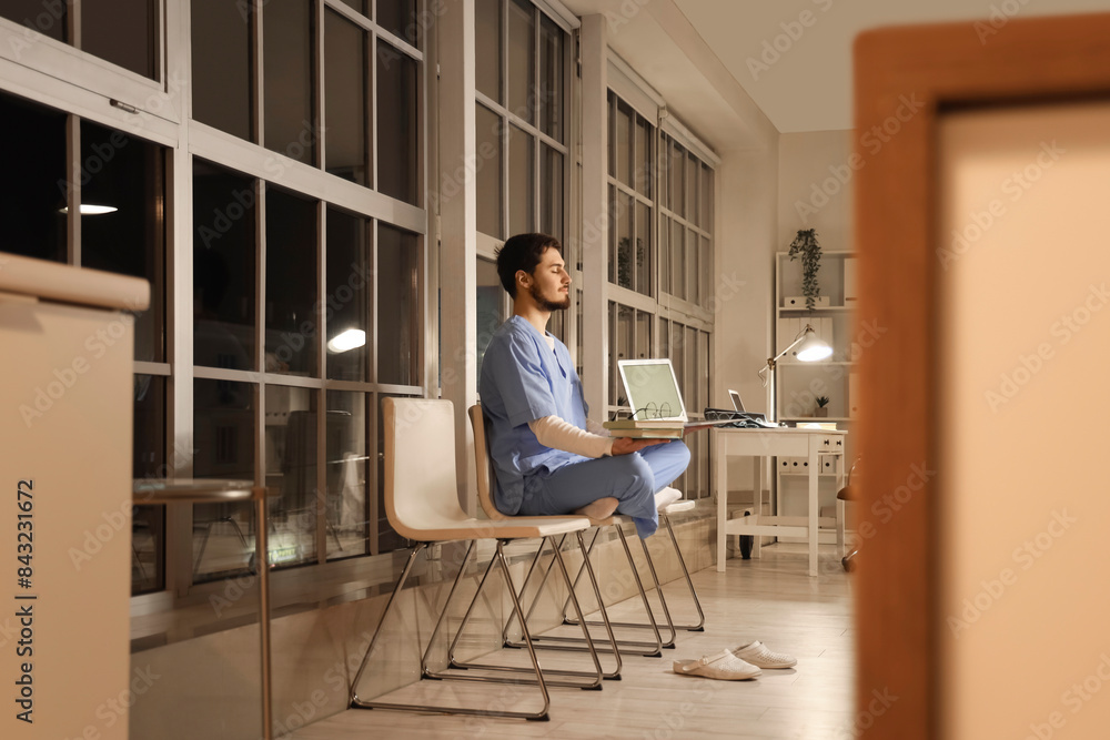 Male nurse with books and laptop meditating at hospital in evening Male nurse with books and laptop meditating at hospital in evening