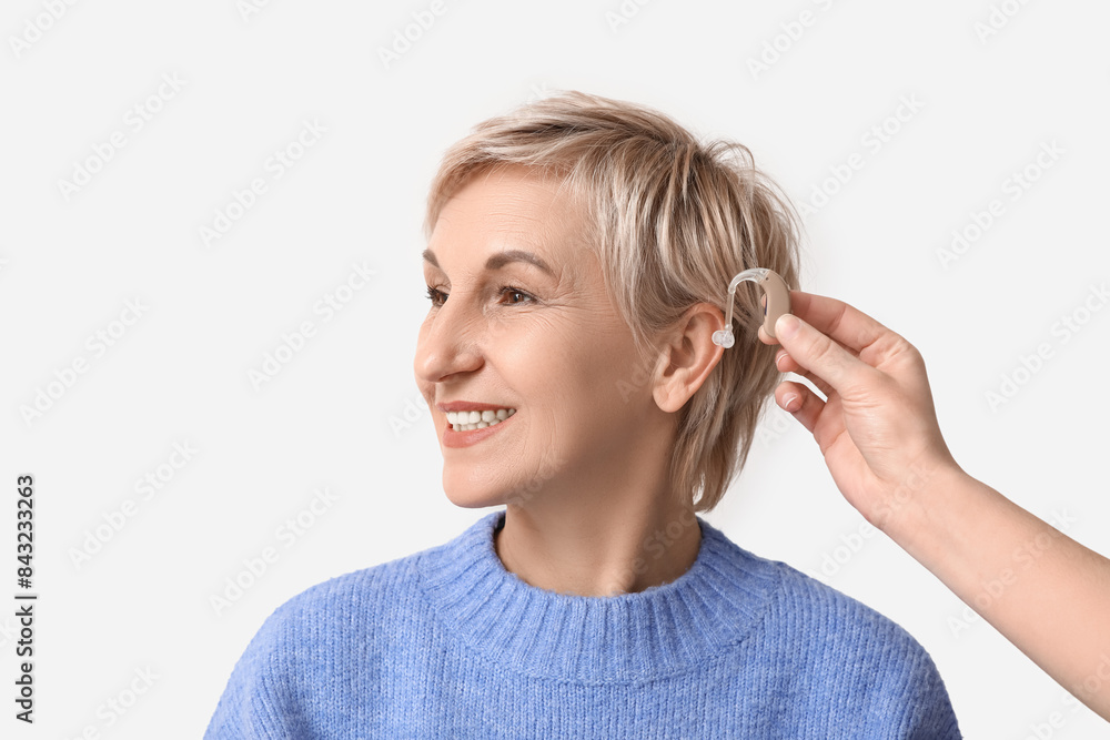 Young woman putting hearing aid in mature woman's ear on white background Young woman putting hearing aid in mature woman's ear on white background