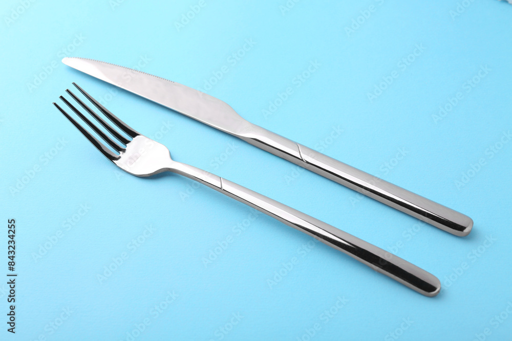 Stylish cutlery. Silver knife and fork on light blue background Stylish cutlery. Silver knife and fork on light blue background