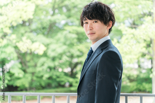 新緑の中にいる若いスーツ姿のビジネスマン・新入社員・転職・就職活動
