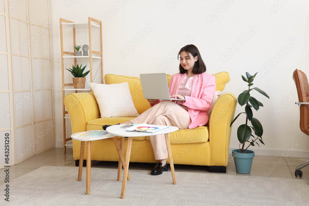 Female interior designer working with laptop on sofa in office Female interior designer working with laptop on sofa in office