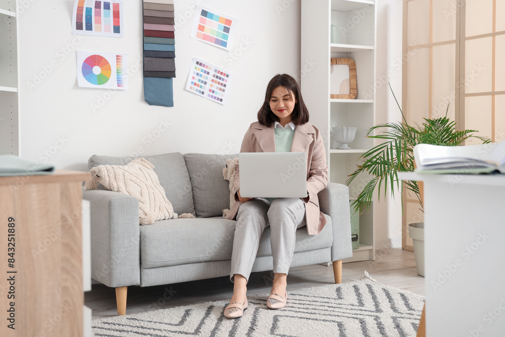 Beautiful interior designer working with laptop on sofa in office Beautiful interior designer working with laptop on sofa in office