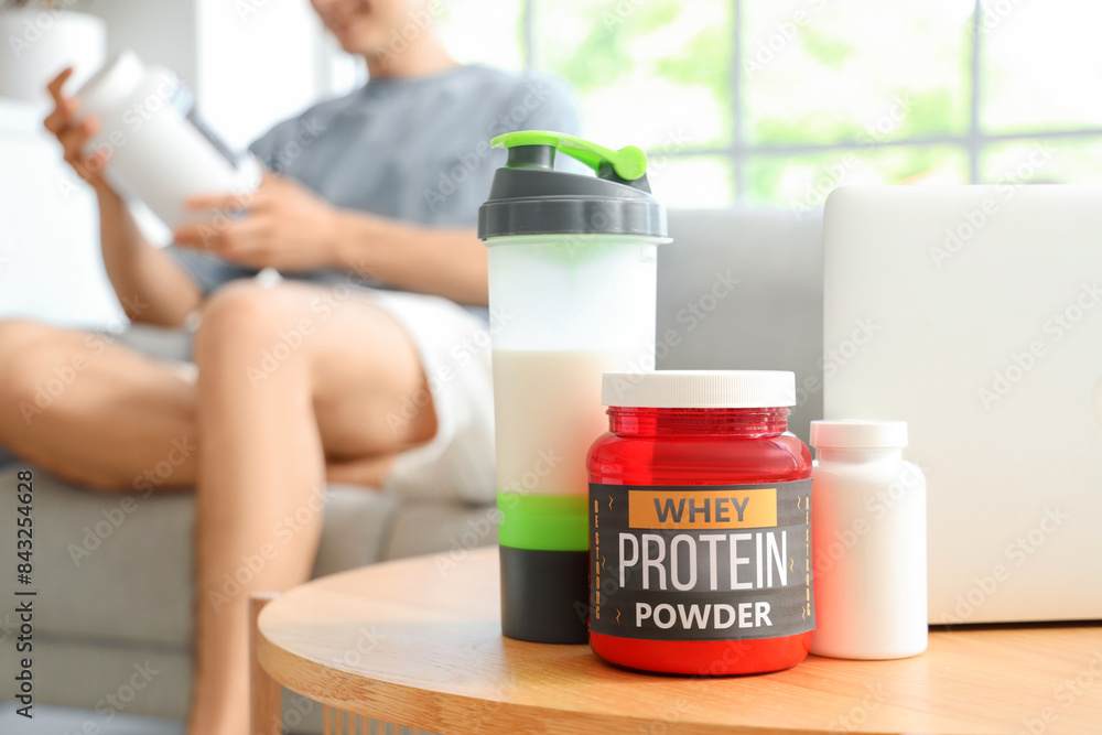 Protein powder with shake, pill bottle and laptop on table of sporty man at home, closeup Protein powder with shake, pill bottle and laptop on table of sporty man at home, closeup