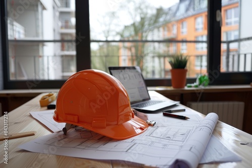 An engineer's workspace with a safety helmet, blueprints, and a laptop photo