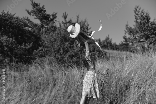 Woman in elegant dress and hat standing in tall grass, embodying timeless beauty and gracefulness of nature and fashion trends photo