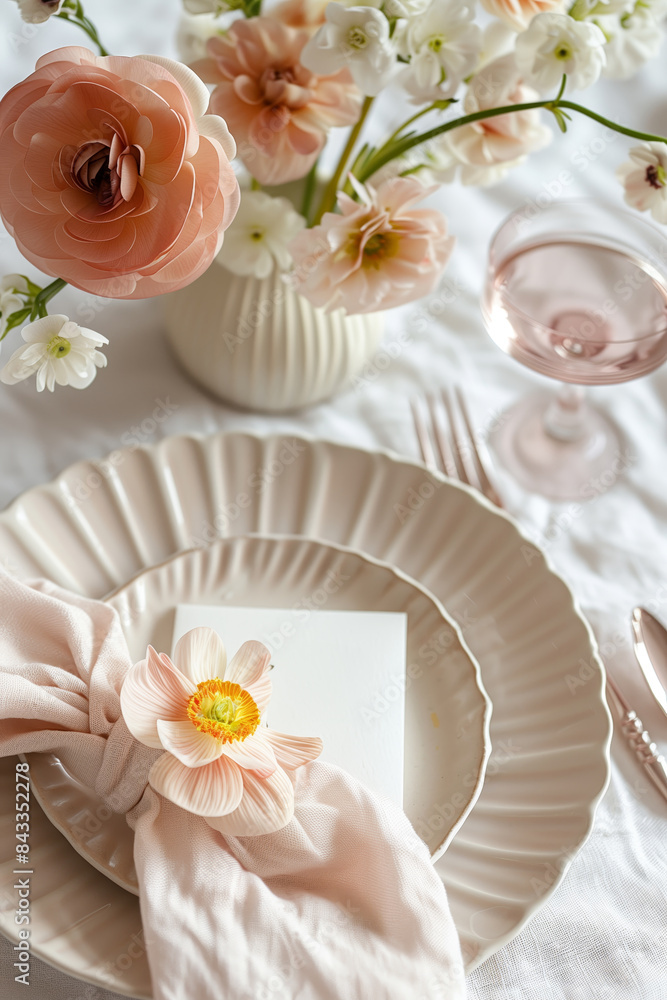 A beautifully arranged table setting featuring delicate flowers in a vase, elegant plates, a pink napkin, and a wine glass.
