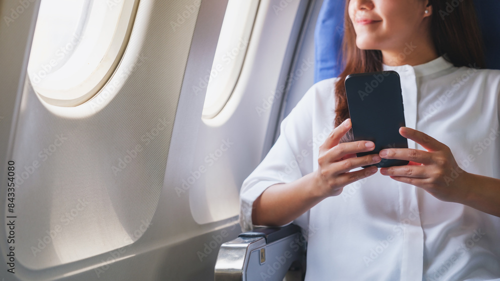 Closeup image of a woman holding and using mobile phone while traveling on an airplane Closeup image of a woman holding and using mobile phone while traveling on an airplane