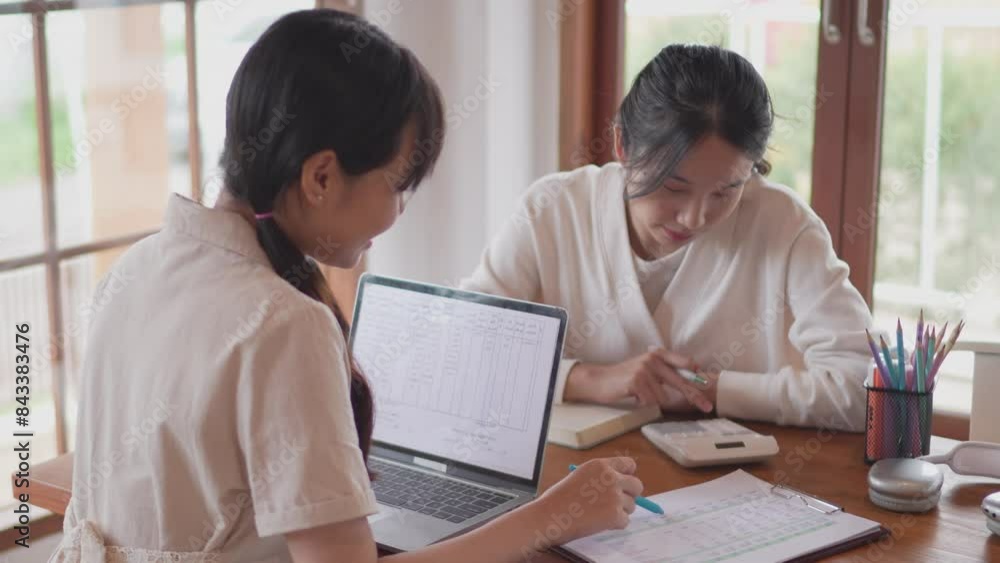 Two Asian university female friends are studying together by discussing the course content and solving statistics problems using a calculator at her home Two Asian university female friends are studying together by discussing the course content and solving statistics problems using a calculator at her home