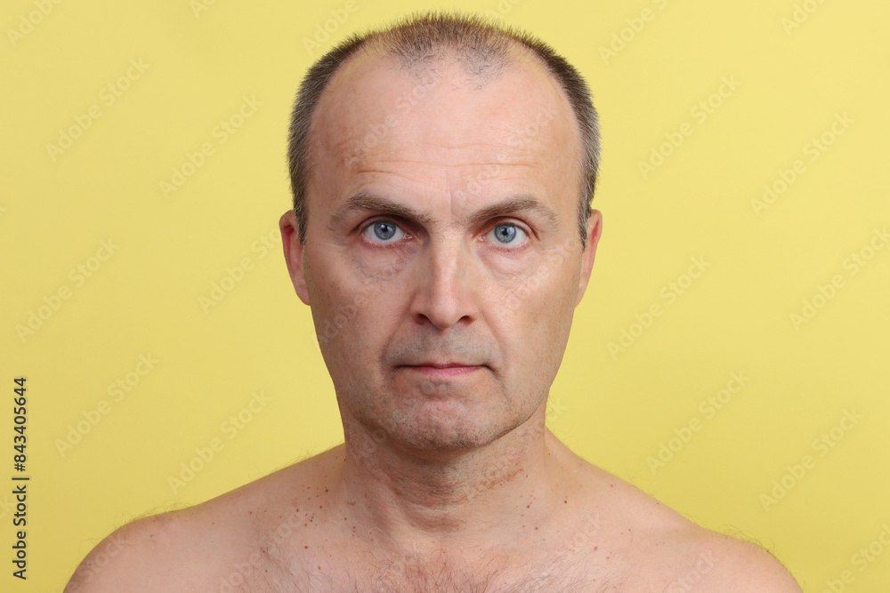Obraz premium A man 45-55 years old without clothes with a hairy chest on a yellow background.