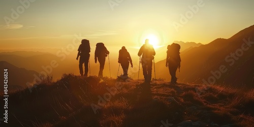 Five hikers walk in silhouette on a mountain ridge as the sun rises behind them