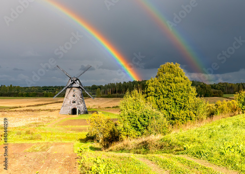 Rainbow above forest and agricultural field with old windmill