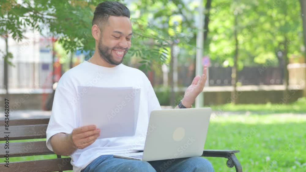 Middle Aged Man Celebrating while working on Documents and Laptop Sitting Outdoor on Bench Middle Aged Man Celebrating while working on Documents and Laptop Sitting Outdoor on Bench