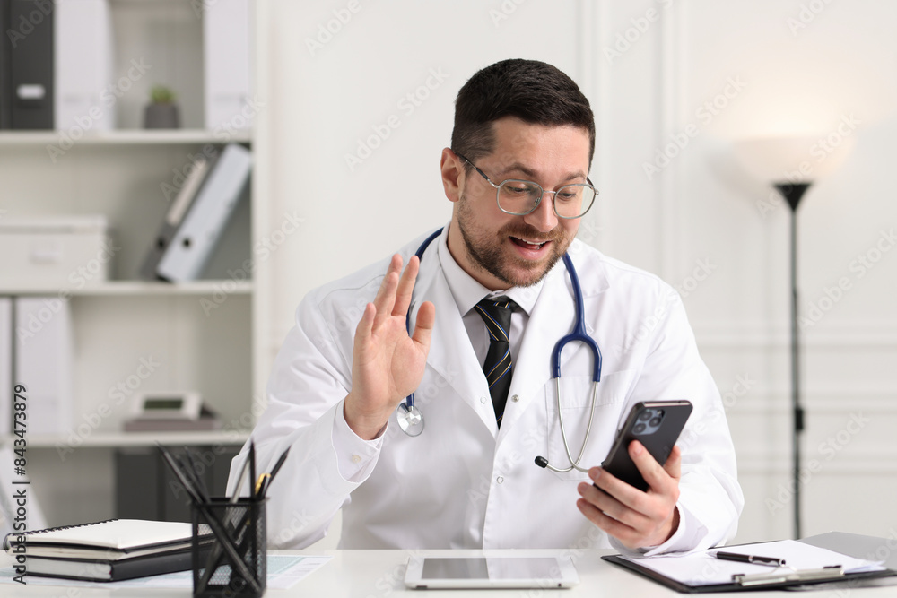 Doctor having online consultation via smartphone at table in clinic Doctor having online consultation via smartphone at table in clinic