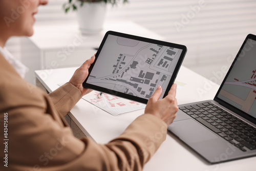 Cartographer working with cadastral map on tablet at white table in office, closeup