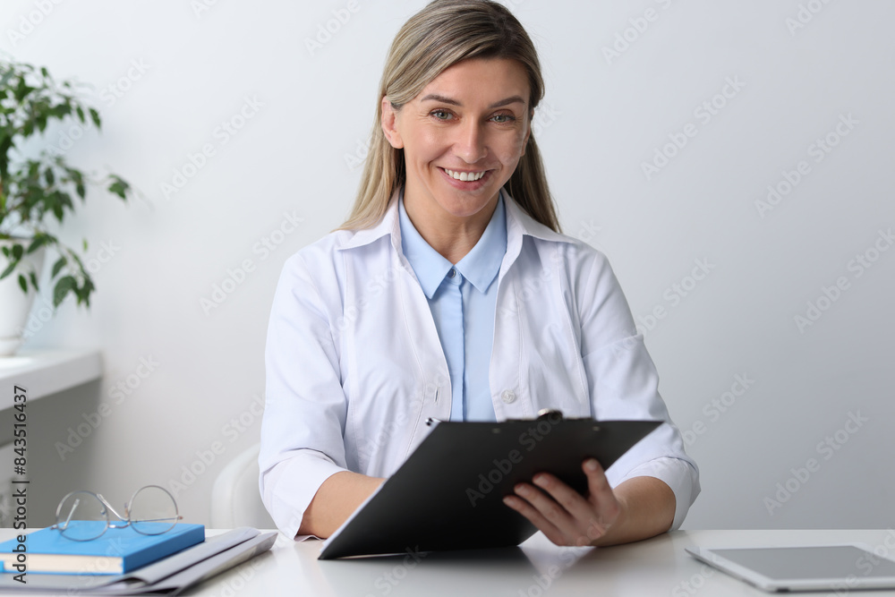 Portrait of happy doctor with clipboard at white table in hospital Portrait of happy doctor with clipboard at white table in hospital