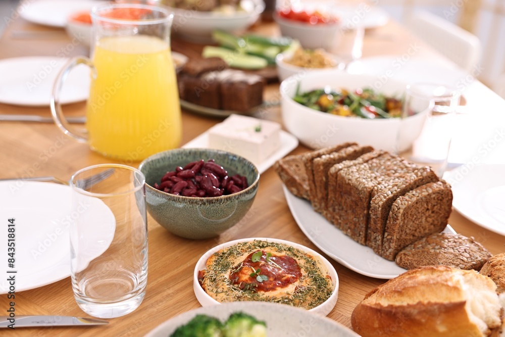 Healthy vegetarian food, jug of juice, glasses, cutlery and plates on wooden table indoors Healthy vegetarian food, jug of juice, glasses, cutlery and plates on wooden table indoors
