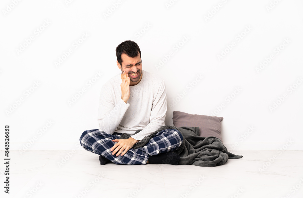 Caucasian man in pajamas sitting on the floor at indoors with toothache Caucasian man in pajamas sitting on the floor at indoors with toothache