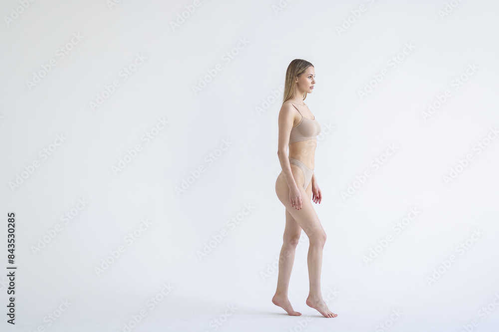 Fototapeta premium Perfect body shape. Full-length portrait of woman with slim fit figure in gray inner wear posing on grey background.
