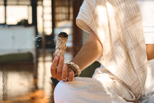 Yogi woman holding scented herbal stick in hand doing yoga breathing exercises. Burning aromatic incense smoky stick with meditating lady close up background. Aromatherapy smoke for healing practices.