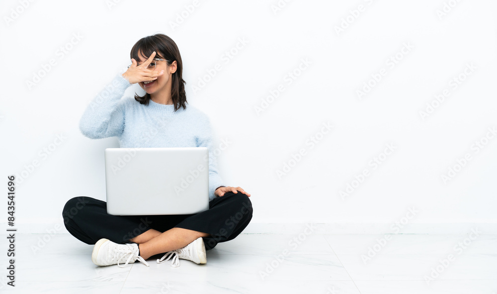 Young mixed race woman sitting on the floor with laptop isolated on white background covering eyes by hands and smiling Young mixed race woman sitting on the floor with laptop isolated on white background covering eyes by hands and smiling