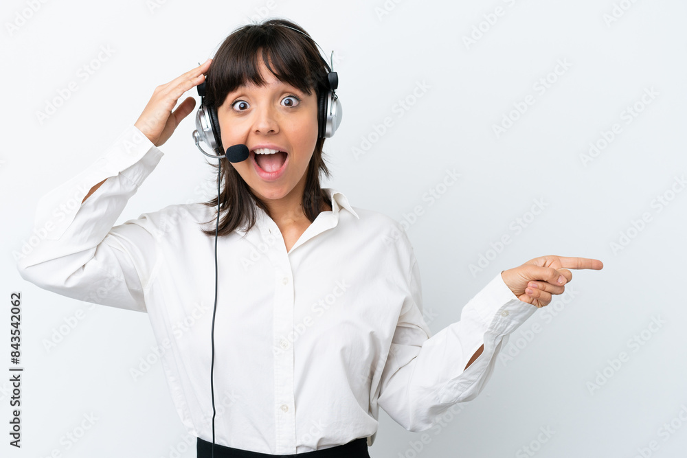 Telemarketer mixed race woman working with a headset isolated on white background surprised and pointing finger to the side Telemarketer mixed race woman working with a headset isolated on white background surprised and pointing finger to the side