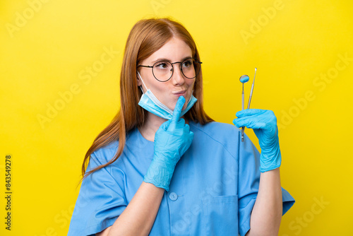 Young redhead Dentist woman isolated on yellow background having doubts while looking up