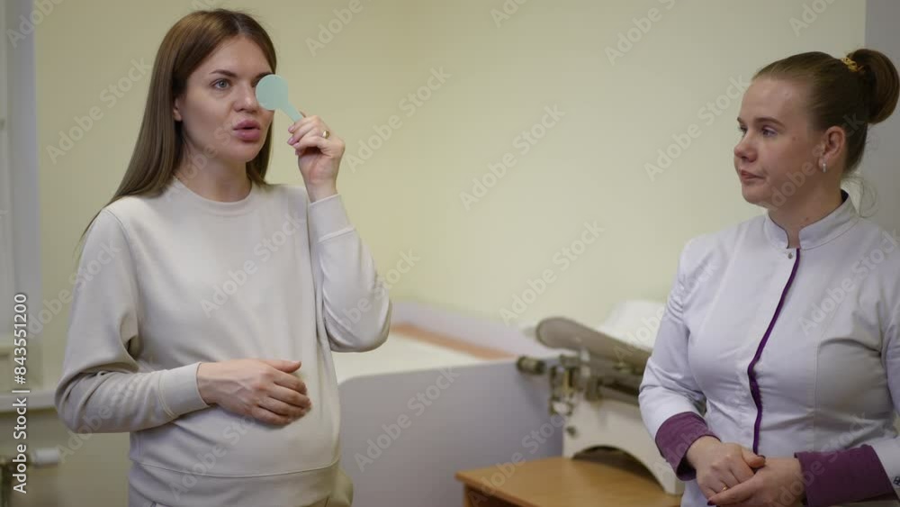 A female physician hands a pregnant patient a plastic eye occluder to properly determine her visual acuity during a physical exam at the clinic A female physician hands a pregnant patient a plastic eye occluder to properly determine her visual acuity during a physical exam at the clinic