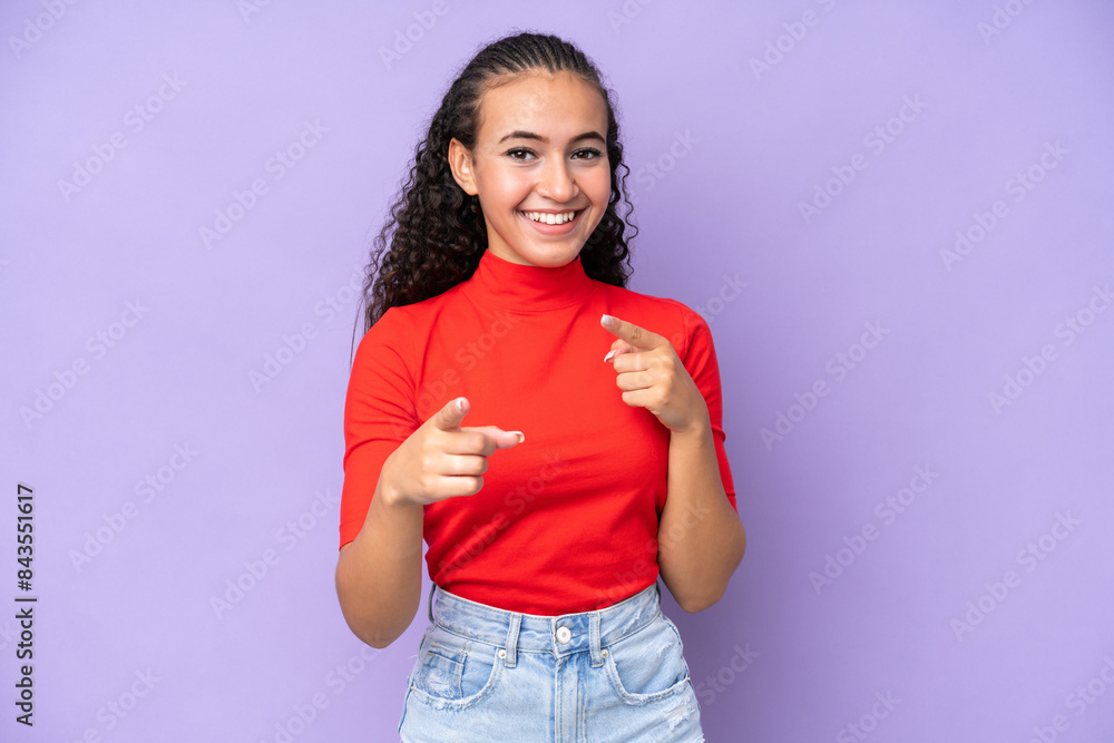Young woman isolated on purple background surprised and pointing front